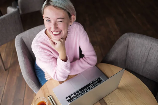 Счастливая улыбающаяся молодая студентка пользуется ноутбуком в библиотеке или кафе . — стоковое фото