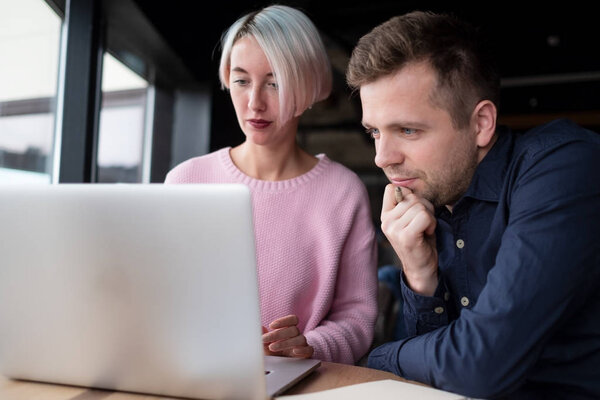 Two coworkers working together on laptop. Pretty experienced woman explaining her inferior how to use computer