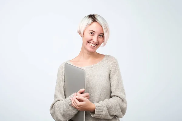 Cheerful young woman with dyed short hair standing, holding laptop computer, making presentation. Stock Picture
