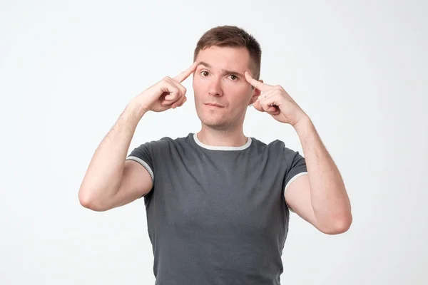 Malheureux jeune homme perplexe pointant sa tête avec les doigts et regardant la caméra . — Photo