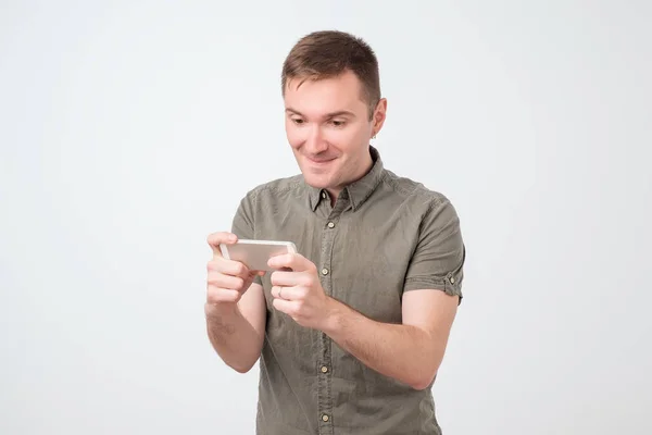 Крупним планом портрет смішного молодого позитивного чоловіка, який грає в ігри на свій смартфон — стокове фото