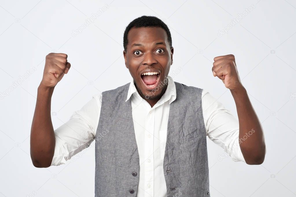 Young african man celebrating victory over gray background