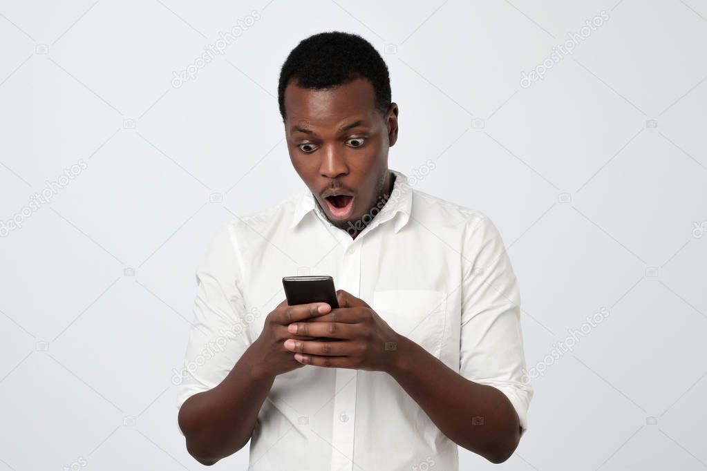African man looking at phone seeing shocking news or photos with surprised emotion on his face
