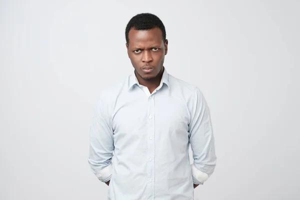 Young african man looks sad and offended, frowned eyebrows, lips pout, wears white shirt — Stock Photo, Image