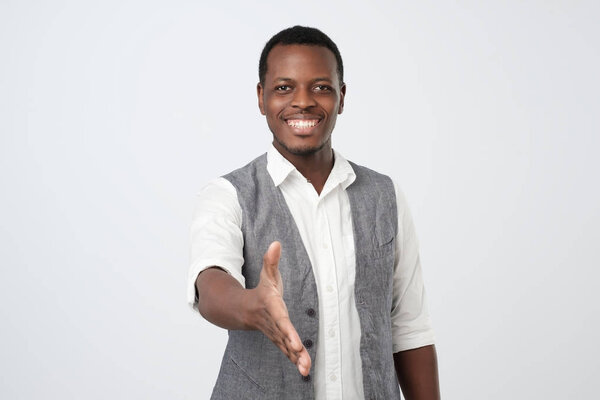 Handsome young african man in white shirt and vest giving his hand for shaking over neutral background