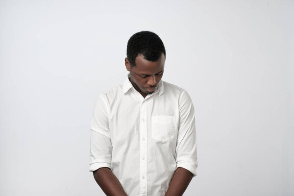 Lack of confidence. Shy young handsome african man feels awkward isolated on grey wall background.