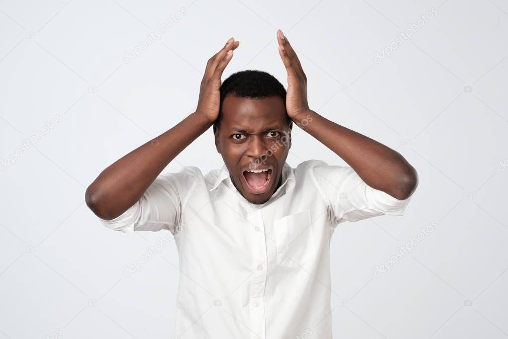 upset angry african man holding hands at his face and shouting isolated over gray wall
