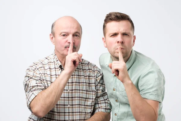 Zwei reife Männer halten den Zeigefinger auf den Lippen, versuchen Verschwörung aufrecht zu erhalten — Stockfoto