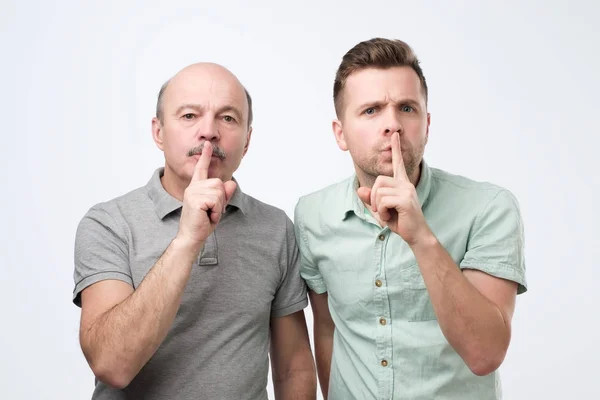 Двоє дорослих чоловіків тримають палець на губах, намагаються зберегти змову — стокове фото