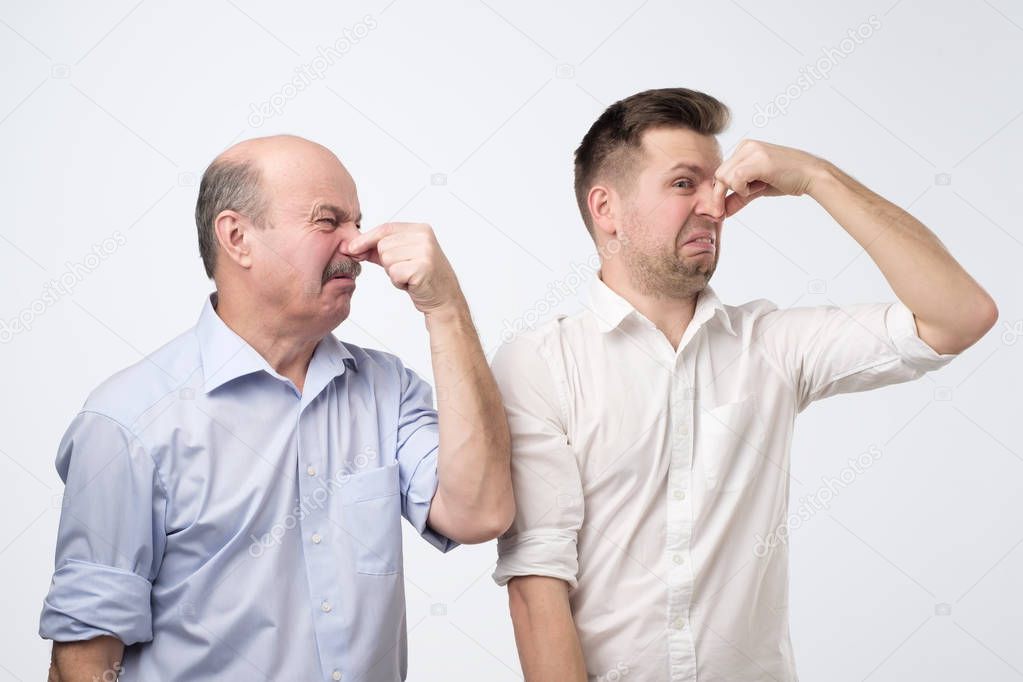 Two men cover their noses due to a bad smell