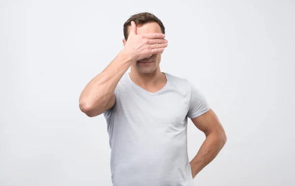 Hombre irreconocible con los ojos tapados mientras se siente avergonzado, de pie contra la pared del estudio en blanco — Foto de Stock