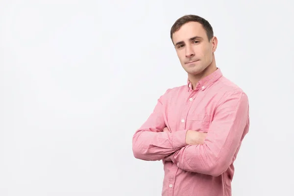 Ernstige jonge man in roze shirt met gekruiste armen over grijze achtergrond — Stockfoto