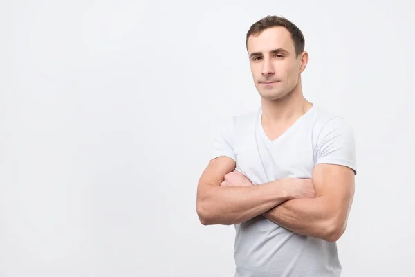 Ernstige jonge man in een wit t-shirt met gekruiste armen — Stockfoto