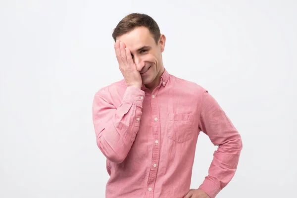 Hombre de camisa rosa mirando a la cámara con astuta expresión divertida, cerrando la boca . — Foto de Stock