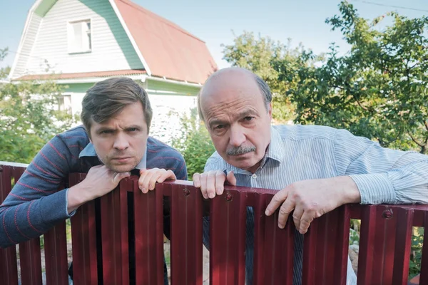 two caucasian men carefully watching over the fence.