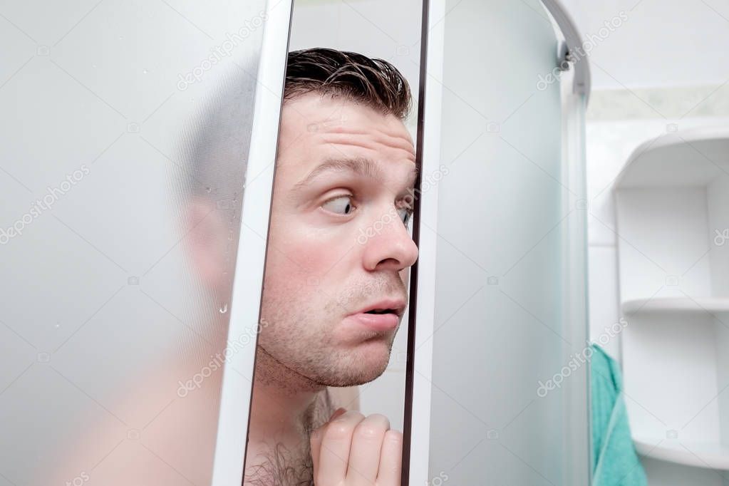 Caucasian young man standing in bathroom with fear in his eyes.