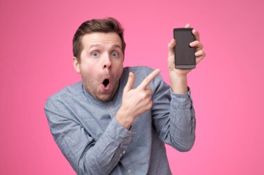 Gadget üzerinde pembe arka plan izole kamera için gösterilen smartphone, holding yakışıklı genç adam.