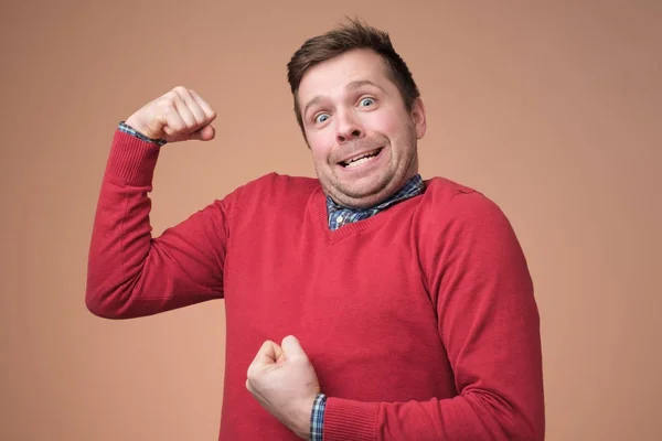 Young funny man in red sweater, shows biceps isolated over white background. — Stock Photo, Image