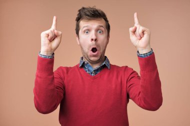 Kırmızı kazaklı hayran yakışıklı adam açılır ağız yaygın olarak, ön plana yükseltir parmak bir fikrim yok gibi