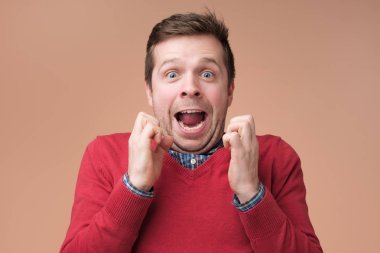 Heyecanlı şaşırmış genç adam kırmızı kazaklı sıkışık tutmak athis yüzler, şok yumruklar