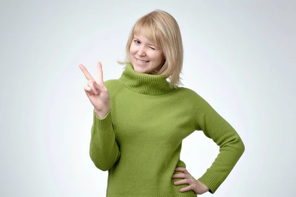 Mosolygós boldog asszony freen pulóver mutatja a győzelem jele, és látszó-on fényképezőgép — Stock Fotó