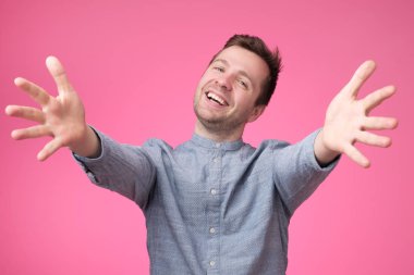 Hoş geldiniz, sizi görmek ne güzel. Yükseltilmiş silah ve mutluluk pembe bir arka plan üzerinde kameraya bakarak mavi tişörtlü adam.