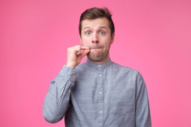 Genç adam ağız kapanış bir işaret gösteren ve sessizlik jest izole pembe bir arka plan üzerinde bir fermuar ağzı kapatma gibi yapıyor
