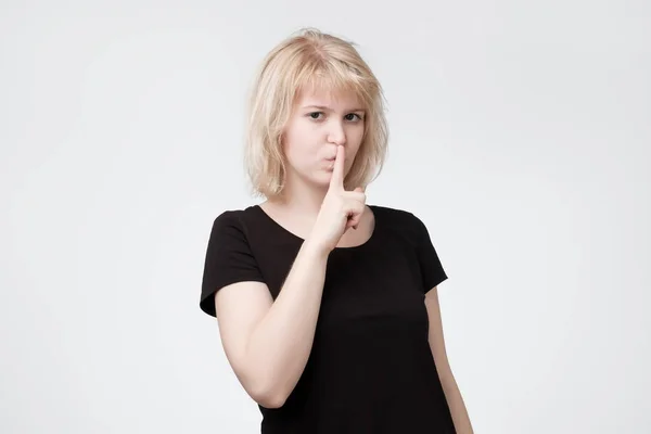 Ovely blonde female asks to keep secret information confidential, dressed in black t-shirt — Stock Photo, Image