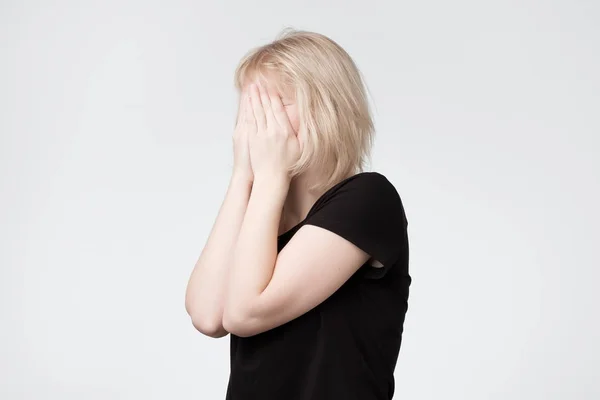 Jonge Europese blonde vrouw in zwarte t-shirtr verbergt haar gezicht — Stockfoto