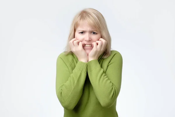 Mujer vistiendo suéter verde asustada, asustada y ansiosa mordiéndose las uñas de los dedos, mirando a la cámara —  Fotos de Stock