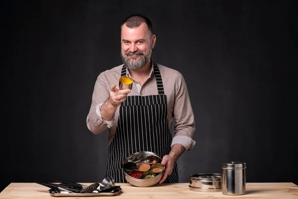 Bearded male chef showing different spices he uses. Secret of delicious food.