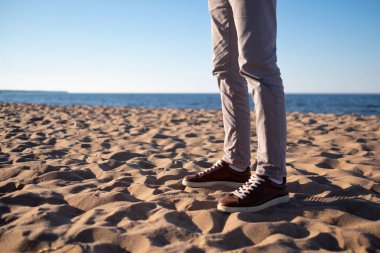 Bacaklar deniz arka plan üzerinde kahverengi spor ayakkabı içinde genç bir adam.