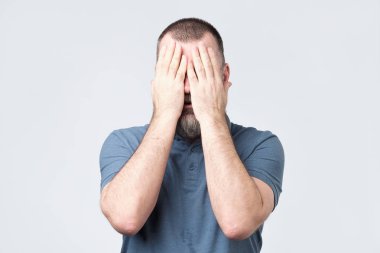 Yüzünü elleriyle kapsayan mavi t-shirt erkekte