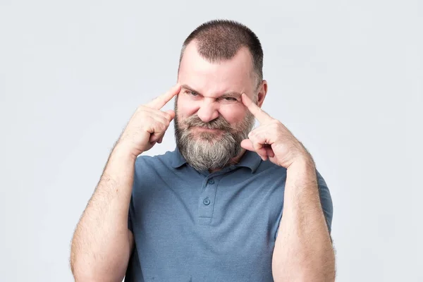 Человек с бородой держит пальцы на висках, пытаясь что-то вспомнить. . — стоковое фото