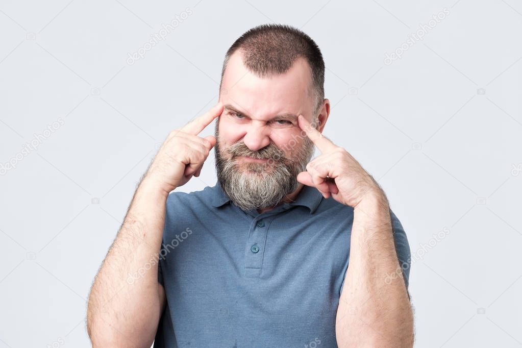 Man with beard holds fingers on temples, trying to remember something.