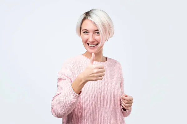 Jovem mulher em suéter rosa com cabelo tingido mostrando polegares para cima — Fotografia de Stock