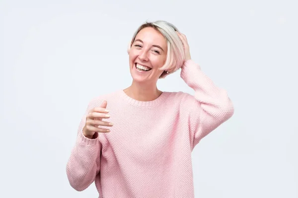 Жінка з фарбованим волоссям, одягнена в рожевий светр, з задоволенням дивиться на камеру, будучи щасливою . — стокове фото