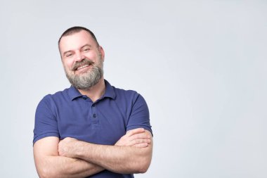 Olgun pozitif adam sakal weairn mavi t-shirt holding el geçti ve beyaz arka plan karşı dururken kamera bakıyor