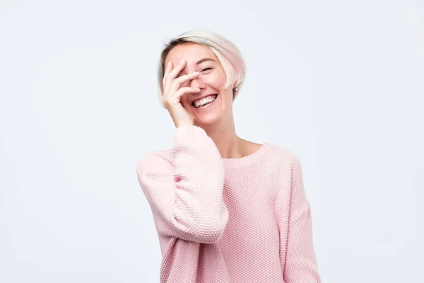 手で顔を閉じて笑っているピンクのセーターに染めたショートヘアの若い女性 それは素晴らしいジョークです — ストック写真