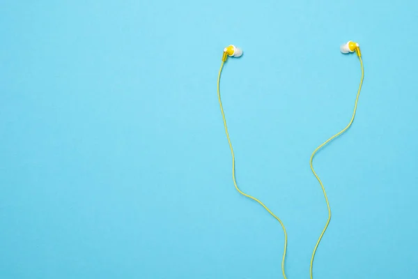Κίτρινο ακουστικά σε μπλε φόντο. Μοντέρνα αξεσουάρ για να ακούτε μουσική. — Φωτογραφία Αρχείου
