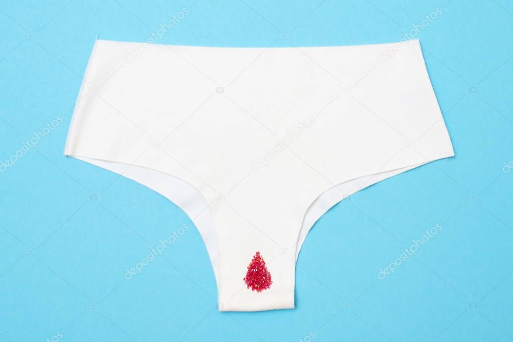 Red drop from beads on pants on blue background. Menstruation period