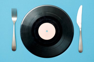 Vinil kaydı çatal ve bıçak üzerinde mavi bir arka plan ile. Zevkli müzik