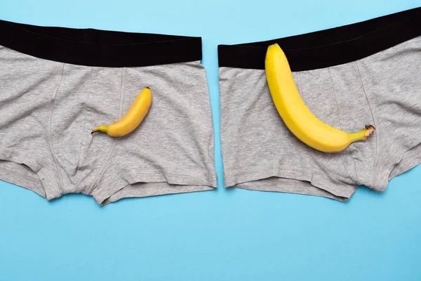 Μωρό μπανάνα σύγκριση μεγέθους με μεγάλη μπανάνα στο αρσενικό εσώρουχα σε μπλε φόντο. — Φωτογραφία Αρχείου