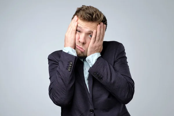Sads young business man in suit, white shirt putting hand on head on grey wall background in studio. — Stock Photo, Image