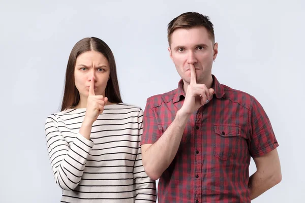 Молода пара показує знак жесту мовчання, який кладе палець у рот на білому тлі — стокове фото