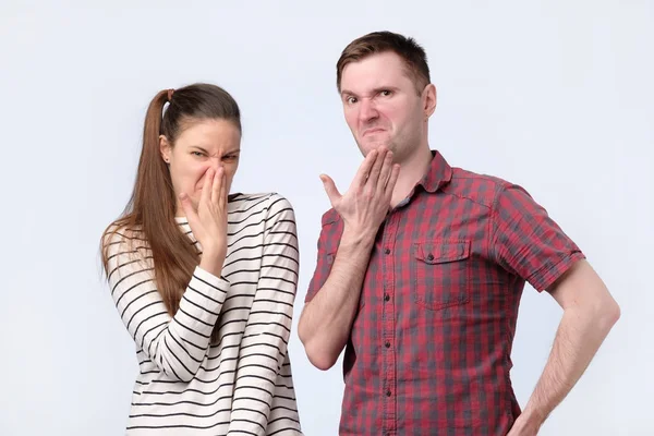 Young cheerful coupleman and woman frowning in disgust their nose from the unpleasant smell. — Stock Photo, Image