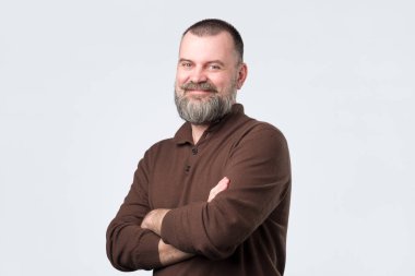 Kahverengi t-shirt sakallı kendinden emin yaşlı adam göğüs üzerinde elleri geçiş ve kamera bakıyor