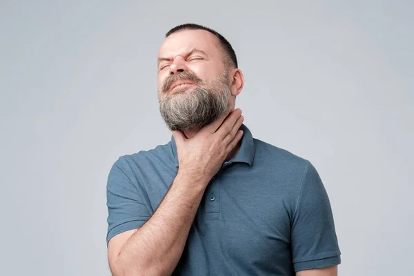 Sjuk man med skägg med smärta i halsen på grå bakgrund. — Stockfoto