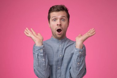 Pembe arka plan üzerinde mavi gömlekli beyaz adamın şok yüzü