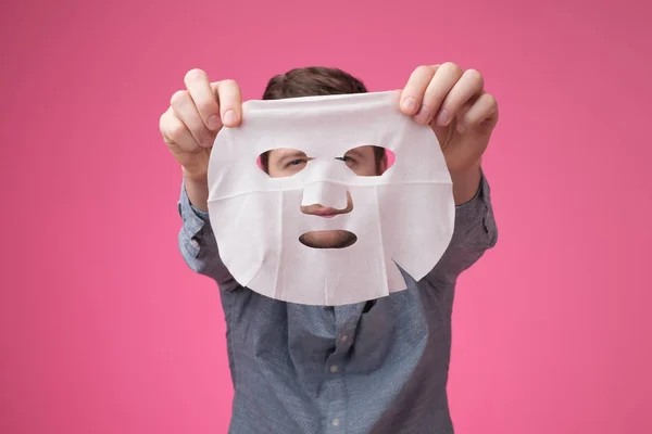 Młody mężczyzna trzyma maskę kosmetyczną blisko kamery. — Zdjęcie stockowe